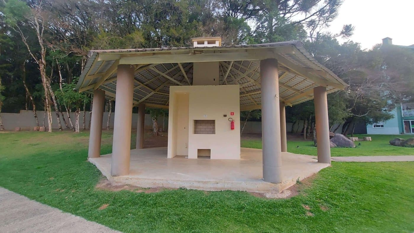 Quiosque de churrasqueira do condomínio, com telhado de madeira e gramado